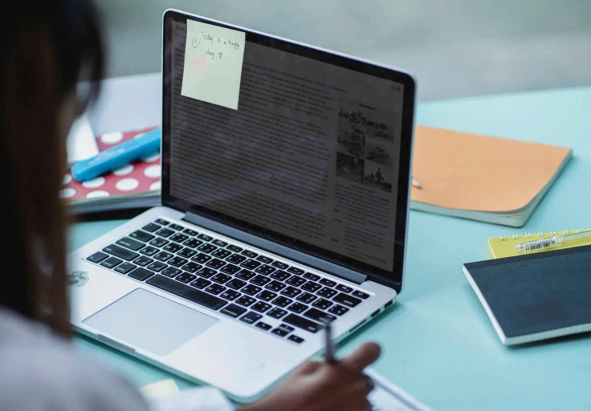 A student reading a long article on a laptop screen with a sticky note attached to the corner
